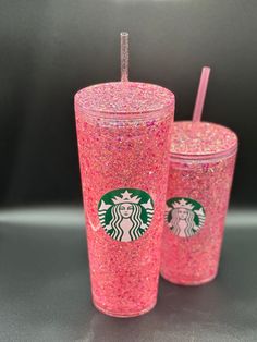 two pink glitter starbucks cups with straws in them sitting on a counter top next to each other