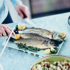 a person cutting fish on a plate with lemons and rosemary garnishes