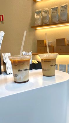 two cups of coffee sitting on top of a white counter next to boxes and bags