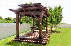 a wooden gazebo sitting on top of a lush green field next to a white fence