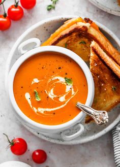 a bowl of tomato soup with grilled bread and cherry tomatoes on the side next to it