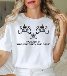 What a fun way to announce a pregnancy!  Player 3 is so cute with the game controllers and the new little player!  Such a fun and funny shower gift, too!  Sure to please the new parents-to-be!  👕 Soft-Washed Garment Dyed  👕 100%  Ring-spun Cotton for extra softness 👕 Pre-shrunk 👕 Relaxed Fit 👕 Wash inside out before wearing the first time 👕 Unisex Sizing: We recommend selecting your favorite-fitting T- shirt       from your closet, and comparing the measurements to the Size Chart       pro White Gamer Tops With Graphic Print, Funny Pregnancy Announcement, Parents To Be, Funny Pregnancy, Matching T Shirts, Pregnancy Announcement Shirt, Game Controllers, Pregnancy Humor, Pregnancy Reveal