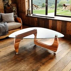 a living room with wooden walls and flooring has a glass table in the middle