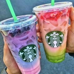 two starbucks drinks with strawberries and blueberries in them are being held by someone's hands