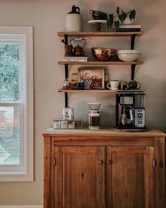 a wooden cabinet sitting next to a window filled with coffee cups and other items on top of it