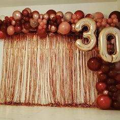 balloons and streamers decorate the backdrop for a 30th birthday party with gold, red and silver decorations