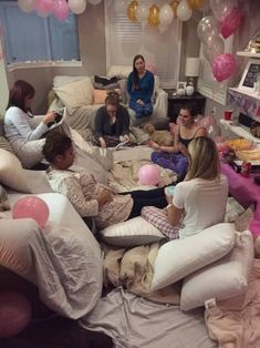 a group of women sitting on top of pillows in a room filled with pink and white balloons