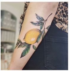 a woman's arm with a lemon and green leaves tattoo on her left forearm