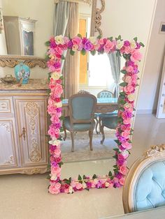 a mirror that has flowers on it in front of a dining room table and chairs