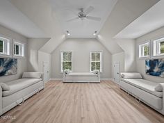 an empty room with white furniture and wood flooring in front of two large windows