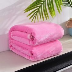 two pink towels sitting on top of a white shelf next to a potted plant