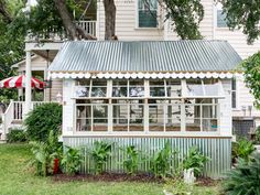 a small house with a metal roof and white trim on the windows, surrounded by lush greenery