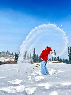 a man in red shirt throwing snow into the air on top of a snowy hill