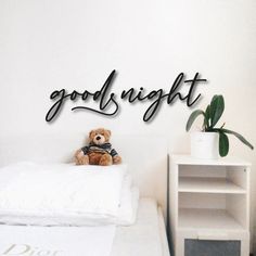 a teddy bear sitting on top of a bed next to a white wall with the words good night