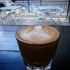 a cup of coffee with a leaf design on the foam in front of some chairs