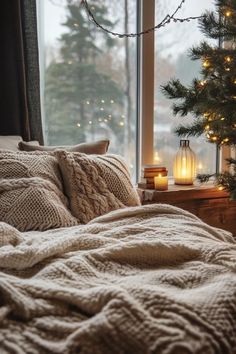 a bed in front of a window with a blanket on it next to a lit christmas tree