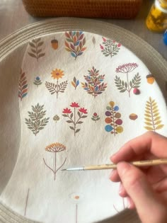 a person is holding a pencil in front of a plate with flowers and leaves on it