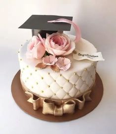 a white cake with pink flowers and a black graduation cap on top