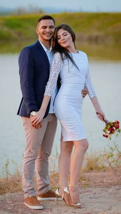 a man and woman standing next to each other in front of a body of water