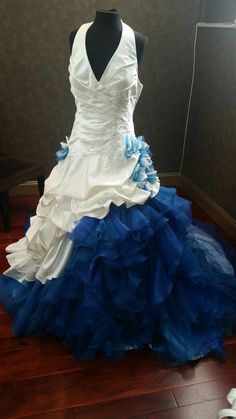 a white and blue wedding dress on display in a room with wood flooring next to a black mannequin