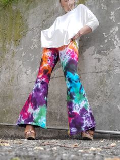 a woman standing in front of a concrete wall wearing colorful pants and a white top