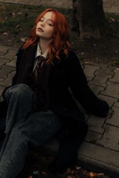 a woman sitting on the ground with her eyes closed, wearing a tie and jeans