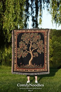 a woman standing in front of a tree with apples on it, holding up a tapestry