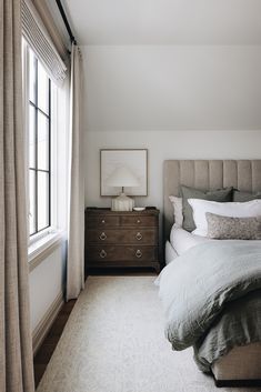 a bed sitting next to a window with curtains on both sides and a dresser in front of it