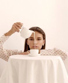 a woman sitting at a table drinking from a white cup with a tea strainer in front of her