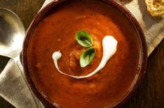 a bowl of soup on a table next to bread and a spoon with a sprig of basil