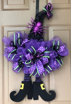 a purple and black halloween wreath hanging on the front door with witch legs attached to it