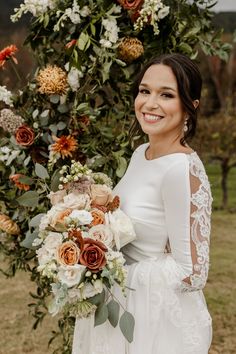 a woman holding a bouquet in front of a flower covered arch with greenery and flowers