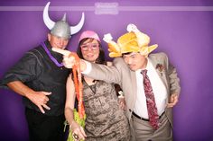 two men and a woman posing for a photo in front of a purple wall with horns on their heads