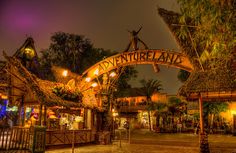 the entrance to adventureland at night with lights on and palm trees in the background