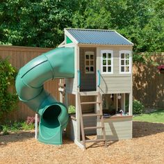 a small wooden play house with a slide and climbing frame in the back yard area