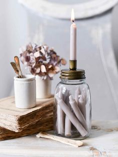 some candles are sitting in a glass jar on a table next to books and flowers