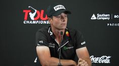 a man sitting at a microphone in front of a black wall with red and white logos