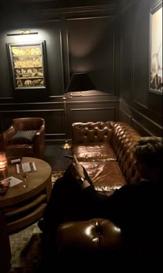 a dimly lit room with leather couches and tables in front of the wall, along with pictures on the walls