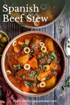 a bowl filled with stew and olives on top of a wooden table next to a spoon