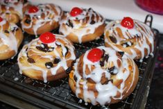 there are many donuts with frosting and cherries on them sitting on a cooling rack