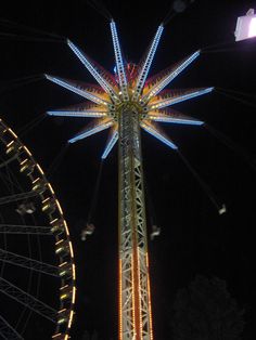 the ferris wheel is lit up at night with bright lights on it's sides