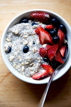 a bowl of oatmeal with strawberries and blueberries on the side