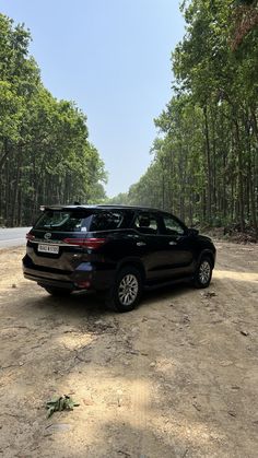 a black suv parked on the side of a dirt road in front of some trees