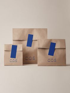 three brown paper bags with blue stickers on them, one has the word cos printed on it