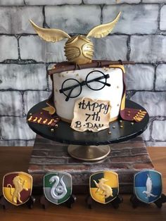 a harry potter birthday cake with glasses on top and gold wings around the edges, surrounded by other decorations