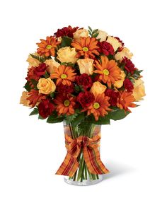 a bouquet of orange and red flowers in a glass vase with a bow on the side