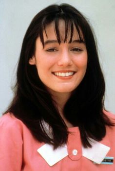 a woman with long black hair wearing a pink shirt and white collared shirt smiling at the camera