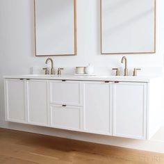 two mirrors are above the double sinks in this white bathroom with wood floors and wooden flooring