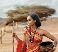 a woman in an orange and red dress holding a stick with camels in the background