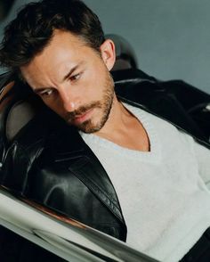 a man sitting in a car looking down at his hand on the steering wheel and wearing a black leather jacket